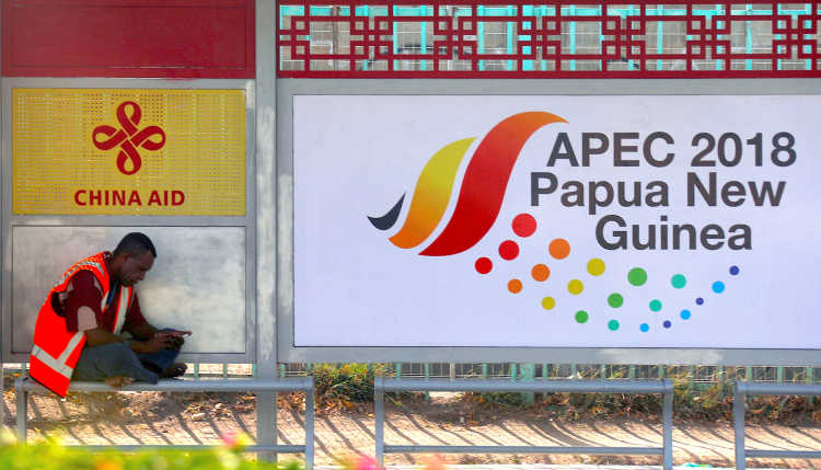 Ein Mann mit Warnweste sitzt im Schatten von Plakaten von China Aid und APEC 2018 Papua-Neuguinea